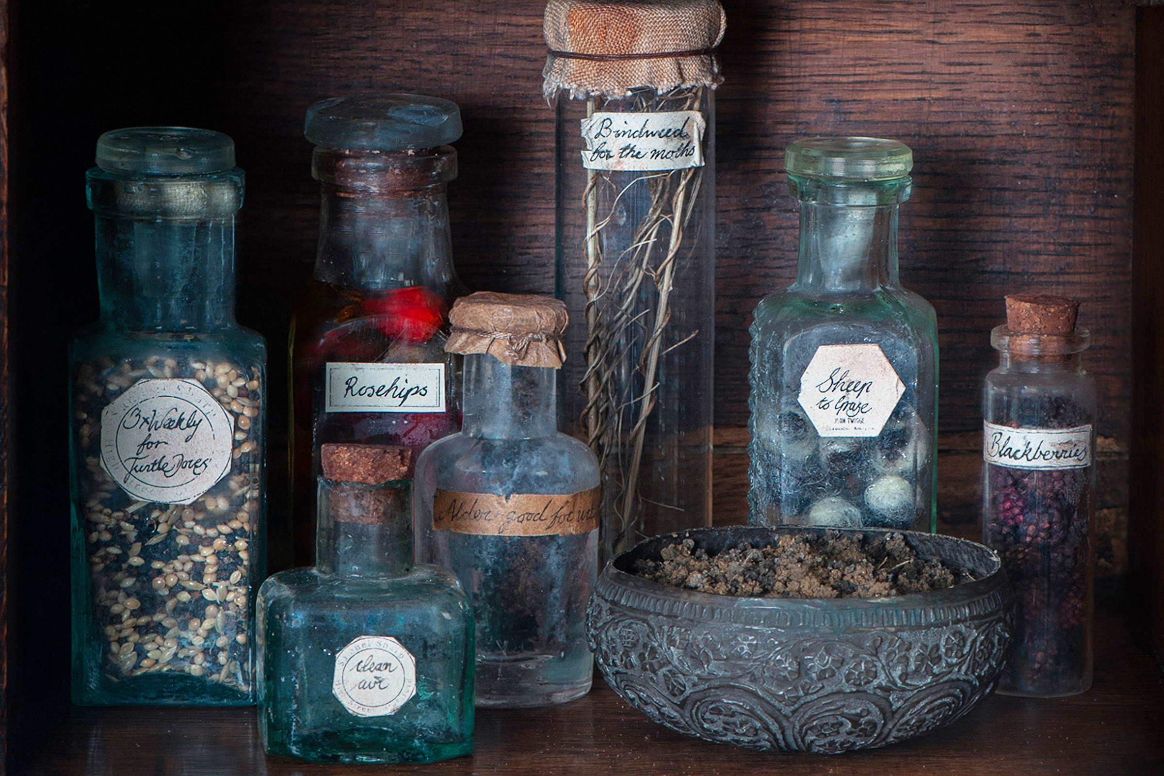 an old-fashioned wooden medicine cabinet. The door is open and inside are jars and pots. On top of the cabinet is a cream ceramic pot with willow branches in it, plus two small glass containers.