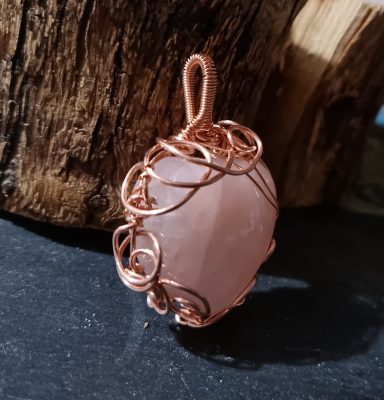 Rose quartz heart wrapped in copper to form a pendant. Side view