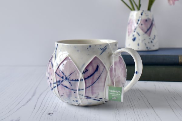 Porcelain wheel thrown mug with slip trailed design. splashy blue and pink glaze. round mug hug.