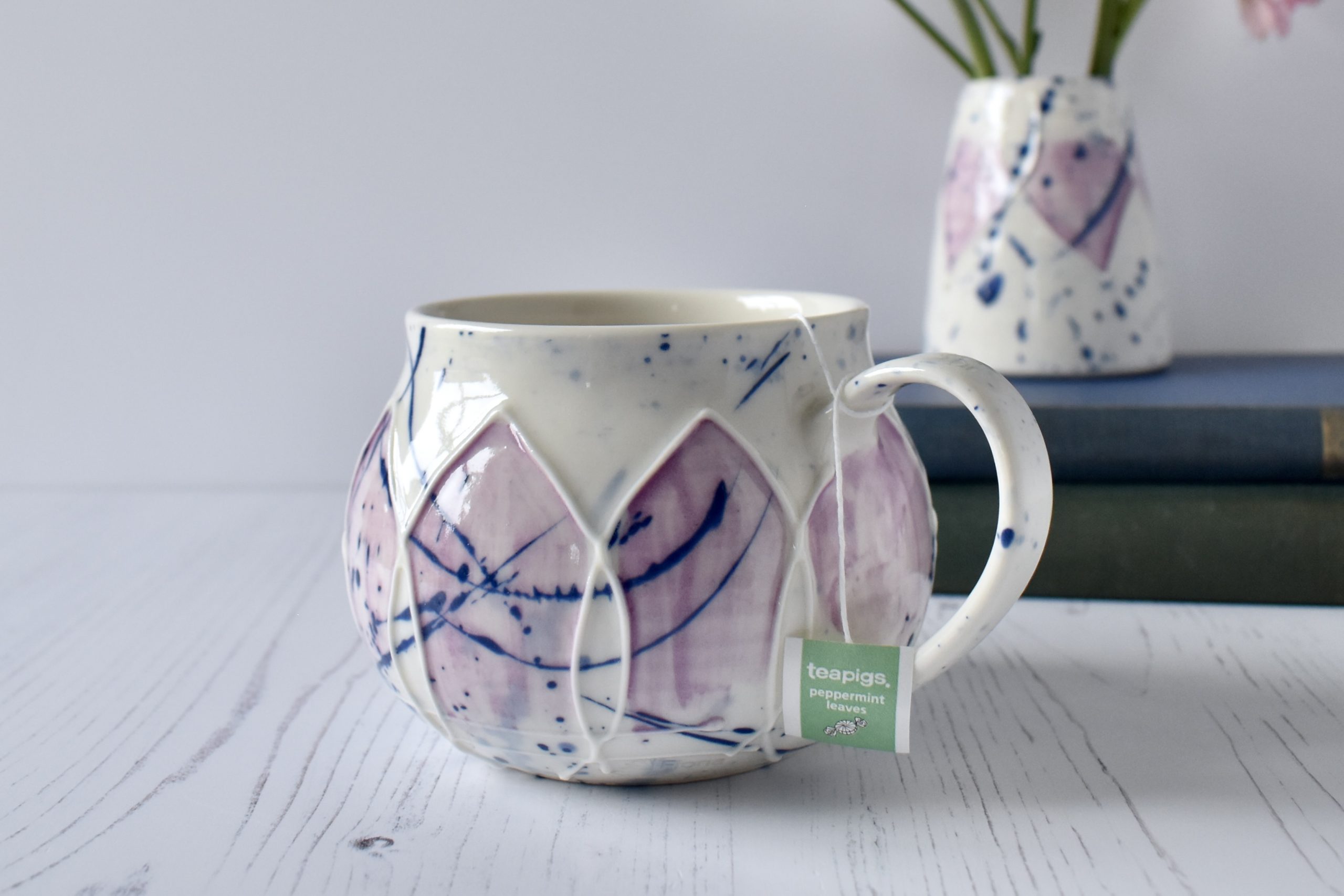 Porcelain wheel thrown mug with slip trailed design. splashy blue and pink glaze. round mug hug.