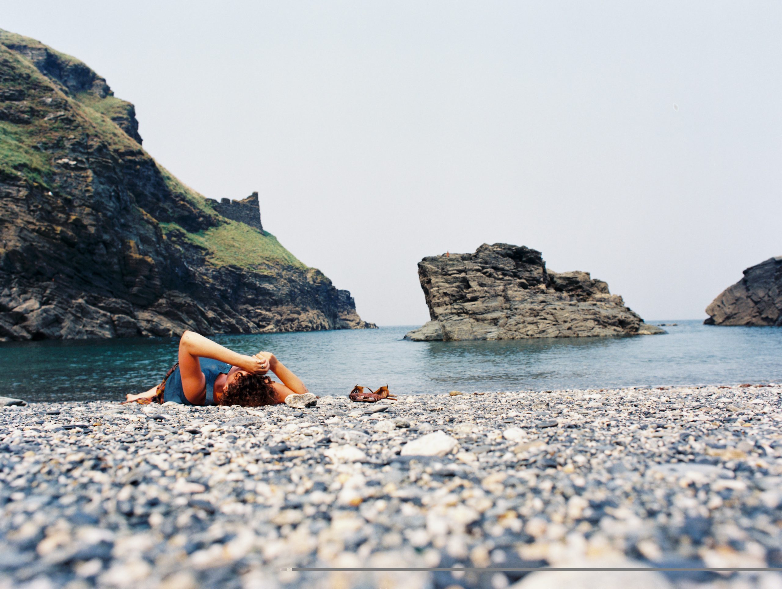 Photo of a man laying on a rocky beach with rocks and sea in the background